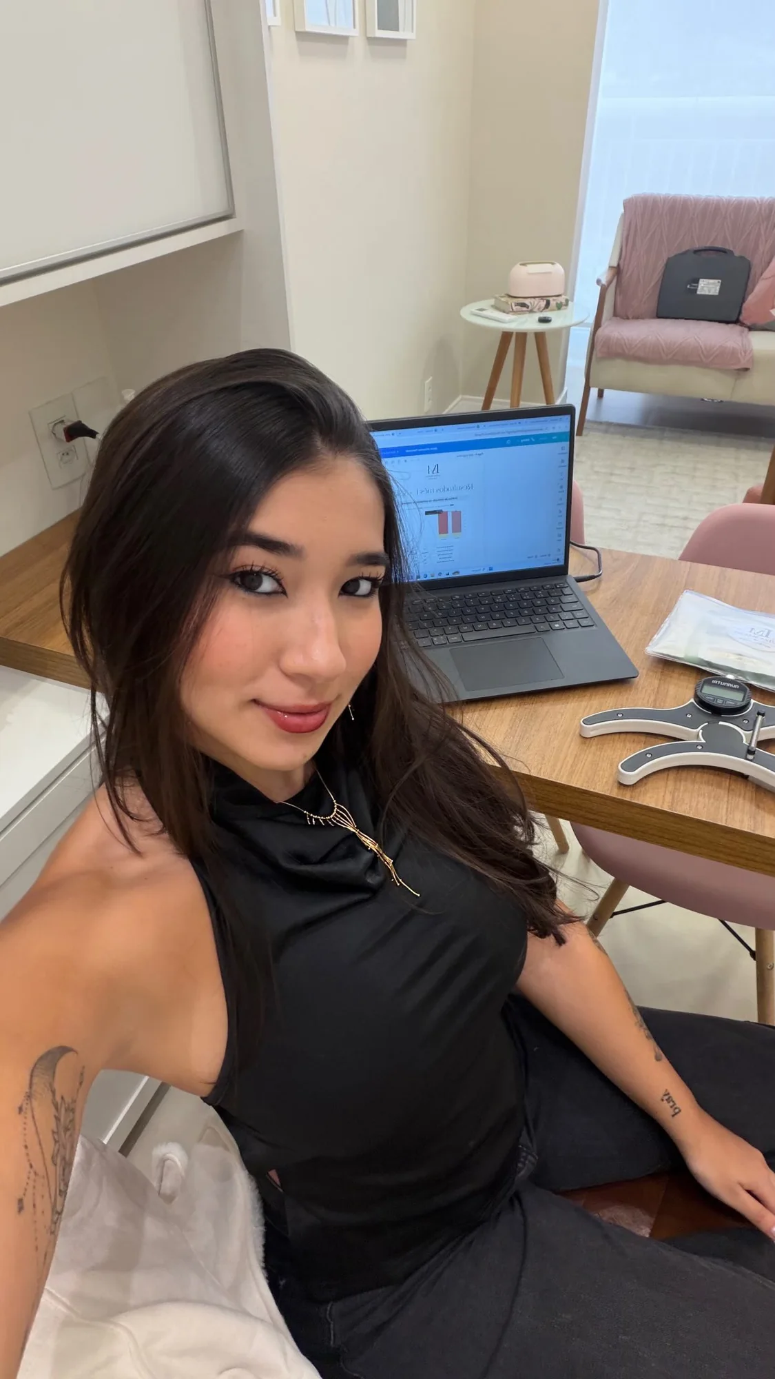 Luiza Maeda sentada à mesa do consultório, com o notebook aberto e um sorriso discreto