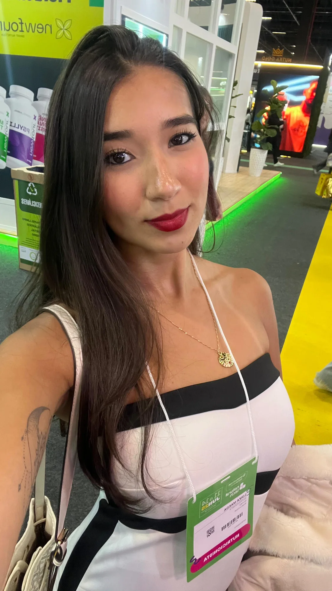 Luiza Maeda em selfie com crachá em uma feira do setor de nutrição